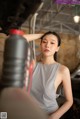 A woman in a gray tank top leaning against a car.