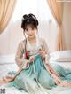 A young girl in a blue and pink hanbok sitting on a bed.