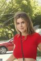 A woman in a red top standing next to a red car.