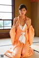 A woman in an orange kimono sitting on a tatami mat.